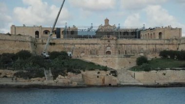 Malta 'daki tarihi bir kalenin resimli kıyı manzarası, hafif rüzgarda dalgalanan bir bayrak.