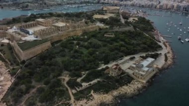 Havadan çekilen bir görüntüde, manzaralı bir marina ve canlı bir şehirle çevrili tarihi bir ada istihkamının altı çiziliyor.