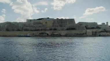 Malta 'daki tarihi bir kalenin resimli kıyı manzarası, hafif rüzgarda dalgalanan bir bayrak.