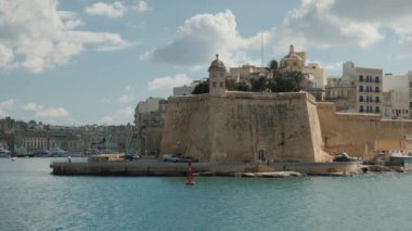 Malta 'daki tarihi bir kalenin resimli kıyı manzarası, hafif rüzgarda dalgalanan bir bayrak.