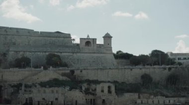 Malta 'daki tarihi bir kalenin resimli kıyı manzarası, hafif rüzgarda dalgalanan bir bayrak.
