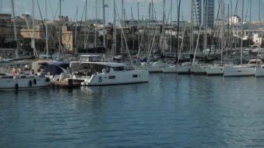 Resimli bir marina, sakin sularda yüzen demirli yatları şehrin ufuk çizgisine karşı sergiliyor.
