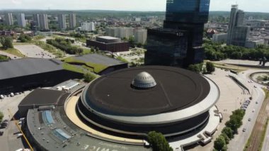 Hava aracı, işlek bir şehirde, gelecekteki gökdelenlerin üzerinde yükselen modern dairesel bir bina sergiliyor.