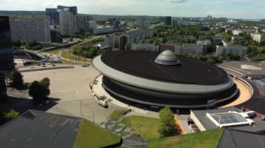 Hava aracı, işlek bir şehirde, gelecekteki gökdelenlerin üzerinde yükselen modern dairesel bir bina sergiliyor.