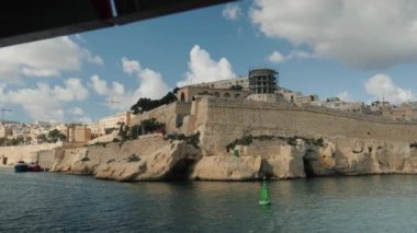 Malta 'daki tarihi bir kalenin resimli kıyı manzarası, hafif rüzgarda dalgalanan bir bayrak.