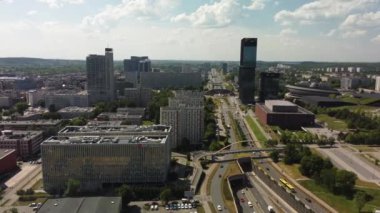 Nefes kesen bir hava manzarası, yemyeşil alanlar ve yüksek gökdelenler içeren canlı ve modern bir şehir manzarası sergiliyor.