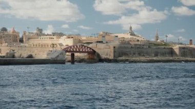 Malta 'daki tarihi bir kalenin resimli kıyı manzarası, hafif rüzgarda dalgalanan bir bayrak.