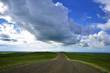 Bir tepenin üstündeki çakıl yolu gökyüzünde kayboluyor, Doğu Montana kırsalında, ufukta ve gökyüzünde büyük bulut görünüyor..