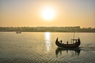 Güneş Moheshkhali, Coxsbazar 'da sakin bir su kütlesinin üzerinde batıyor. Uzaktan bir tekne görülebilir. Gemide birkaç kişi var, suda eğleniyorlar..
