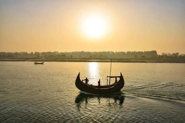 Güneş Moheshkhali, Coxsbazar 'da sakin bir su kütlesinin üzerinde batıyor. Uzaktan bir tekne görülebilir. Gemide birkaç kişi var, suda eğleniyorlar..