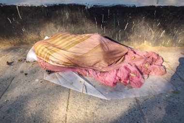 Kadın elinde bir çöp torbasıyla yerde oturuyor.