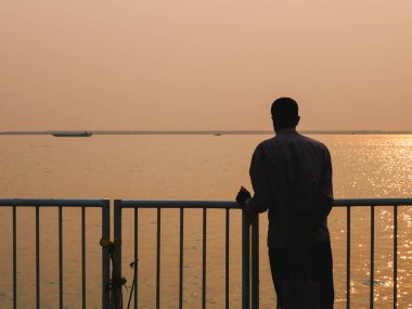 Genç adam gün batımında iskelede oturuyor.