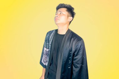 Üzerinde desenli detaylar olan siyah bir kıyafet giyen bir adam, parlak sarı bir arka plan karşısında hayal kırıklığına uğramış veya hayal kırıklığına uğramış bir ifadeyle telefonunu kulağına tutar. Kötü haberlerle ilgili konular, zor konuşmalar, alışkanlık