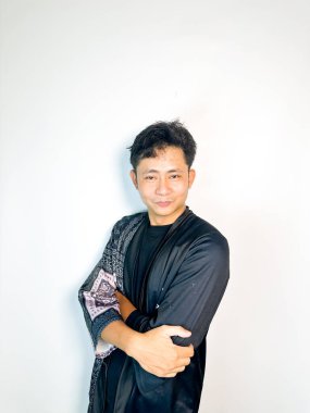 Geleneksel desenli siyah cüppeli genç bir adam başını hafifçe eğerken neşeli bir sırıtış yapar. Yüzündeki ifade eğlence, yaramazlık ya da hafif bir tepki veriyor. Bu da onu mizah, merak ya da iğneleme gibi kavramlar için ideal kılıyor..