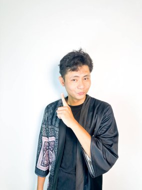 Geleneksel siyah bornoz giyen genç bir adam düşünceli görünürken işaret parmağıyla hareket ediyor. Bu ifade bir fikri veya farkındalığı akla getiriyor, beyin fırtınası, ilham ve problem çözme gibi kavramlara uygun kılıyor..