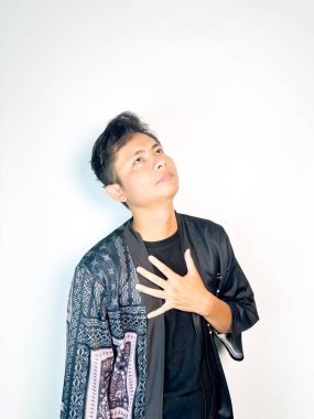 Siyah kimono tarzı bornoz giyen genç bir adam umut dolu ve düşünceli bir ifadeyle elini göğsüne koyar. Vücut dili minnettarlık, rahatlama ya da derin tefekkür iletir. Bu resim fait ile ilgili temalar için mükemmeldir