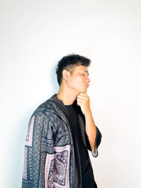 Geleneksel siyah bornoz giyen genç bir adam düşünceli görünürken işaret parmağıyla hareket ediyor. Bu ifade bir fikri veya farkındalığı akla getiriyor, beyin fırtınası, ilham ve problem çözme gibi kavramlara uygun kılıyor..