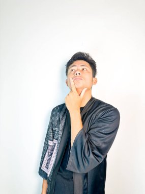 Geleneksel siyah bornoz giyen genç bir adam düşünceli görünürken işaret parmağıyla hareket ediyor. Bu ifade bir fikri veya farkındalığı akla getiriyor, beyin fırtınası, ilham ve problem çözme gibi kavramlara uygun kılıyor..