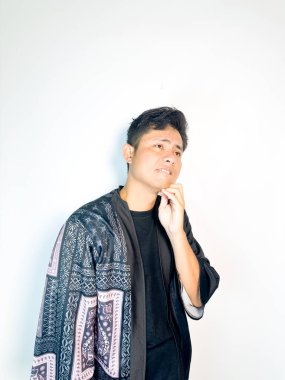 Geleneksel siyah bornoz giyen genç bir adam düşünceli görünürken işaret parmağıyla hareket ediyor. Bu ifade bir fikri veya farkındalığı akla getiriyor, beyin fırtınası, ilham ve problem çözme gibi kavramlara uygun kılıyor..