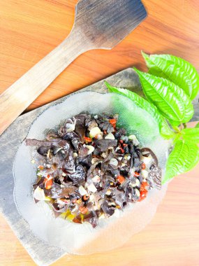 Kırmızı biber, sarımsak ve ahşap bir tahta üzerinde taze bitkisel yapraklarla baharatlı siyah mantar salatası içeren geleneksel bir Asya yemeği. Mutfak temaları, Asya mutfağı, sağlıklı yiyecekler ve vejetaryen yemekler için mükemmel..