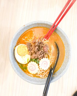 Haşlanmış yumurta, balık köftesi, sebze ve yemek çubuklarıyla sıcak ve baharatlı erişte kasesinin üst görüntüsü. Tahta bir masada servis edilmiş. Japon mutfağı, konforlu yemekler, Asya yemekleri ve erişte çorbası gibi konular için mükemmel..