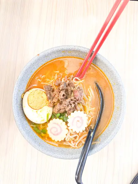 Haşlanmış yumurta, balık köftesi, sebze ve yemek çubuklarıyla sıcak ve baharatlı erişte kasesinin üst görüntüsü. Tahta bir masada servis edilmiş. Japon mutfağı, konforlu yemekler, Asya yemekleri ve erişte çorbası gibi konular için mükemmel..