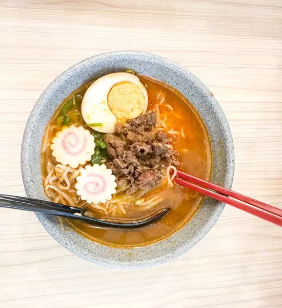 Haşlanmış yumurta, balık köftesi, sebze ve yemek çubuklarıyla sıcak ve baharatlı erişte kasesinin üst görüntüsü. Tahta bir masada servis edilmiş. Japon mutfağı, konforlu yemekler, Asya yemekleri ve erişte çorbası gibi konular için mükemmel..