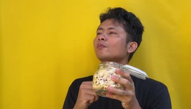 Genç adam cam kavanozda muz yiyor.