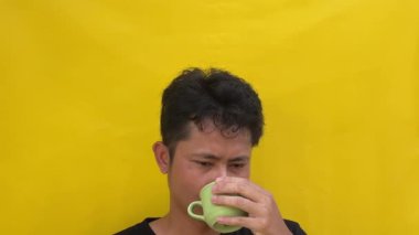 Genç adam sarı arka planda kahve içiyor.