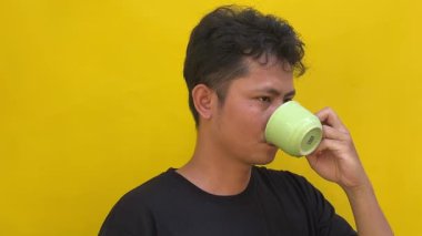 Genç adam sarı arka planda sıcak kahve içiyor.