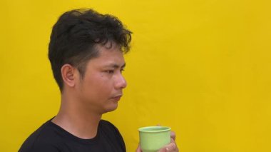 Asyalı yakışıklı adam sıcak kahve veya sarı renkli çay içiyor..