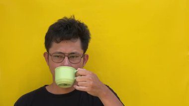 Genç adam sarı arka planda bir fincan kahve içiyor.