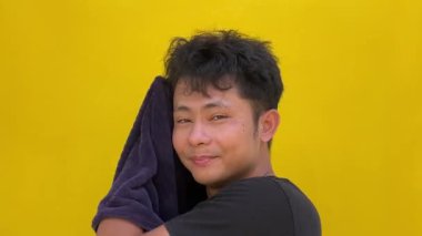 Sarı gömlekli genç Asyalı adam gülümsüyor ve kameraya bakıyor..