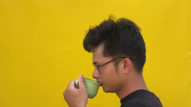 Yeşil arka planda sarı kahve fincanı olan genç Asyalı erkek.
