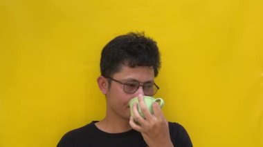 Genç Asyalı bir adam sarı bardağı tutuyor ve izole edilmiş beyaz arka plana bakarken düşünüyor