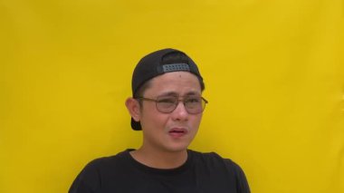 Gözlüklü ve sarı tişörtlü bir adam kameraya bakıyor, gülümsüyor, dilini gösteriyor.