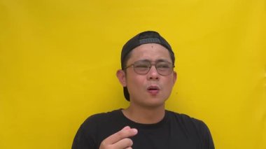 Siyah gömlekli, sarı gözlüklü, siyah arka planlı Asyalı genç adam.