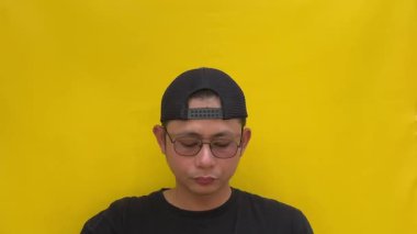 Sarı arka planda sarı tişörtlü Asyalı genç bir adamın portresi.