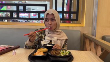 Siyah başörtüsü takan ve sandviç yiyen genç bir Asyalı kadın.