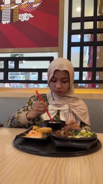 Bir kafede pirinç yiyen Asyalı genç Müslüman kadının portresi..