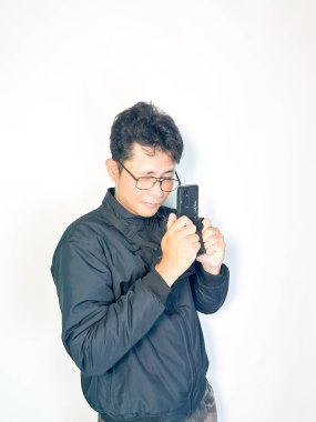 Beyaz gömlek ve mavi kot pantolon giyen, gri arka planda akıllı telefonu olan Asyalı genç adam..