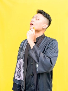 Asyalı genç bir adamın portresi sarı bir jiletle yüzünü tıraş ediyormuş gibi yapıyor, acı çekiyormuş gibi komik bir yüz ifadesi takınıyor, parlak sarı bir arka plana karşı..