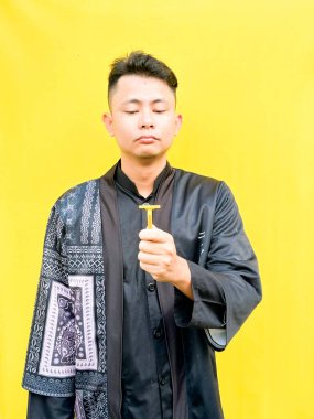 Asyalı genç bir adamın portresi sarı bir jiletle yüzünü tıraş ediyormuş gibi yapıyor, acı çekiyormuş gibi komik bir yüz ifadesi takınıyor, parlak sarı bir arka plana karşı..