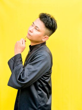 Asyalı genç bir adamın portresi sarı bir jiletle yüzünü tıraş ediyormuş gibi yapıyor, acı çekiyormuş gibi komik bir yüz ifadesi takınıyor, parlak sarı bir arka plana karşı..
