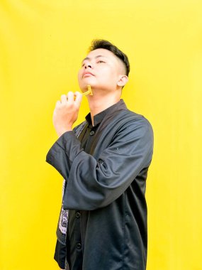 Asyalı genç bir adamın portresi sarı bir jiletle yüzünü tıraş ediyormuş gibi yapıyor, acı çekiyormuş gibi komik bir yüz ifadesi takınıyor, parlak sarı bir arka plana karşı..