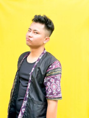 Modern etnik esinlenilmiş bir kıyafet giyen genç bir Asyalı 'nın portresi, parlak sarı bir arkaplan önünde dururken şüpheli ya da meraklı bir görünüm veriyor. Duygular, ruh hali ifadesi gibi kavramlar için mükemmel..