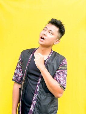 Modern etnik esinlenilmiş bir kıyafet giyen genç bir Asyalı 'nın portresi, parlak sarı bir arkaplan önünde dururken şüpheli ya da meraklı bir görünüm veriyor. Duygular, ruh hali ifadesi gibi kavramlar için mükemmel..