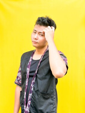 Modern etnik esinlenilmiş bir kıyafet giyen genç bir Asyalı 'nın portresi, parlak sarı bir arkaplan önünde dururken şüpheli ya da meraklı bir görünüm veriyor. Duygular, ruh hali ifadesi gibi kavramlar için mükemmel..