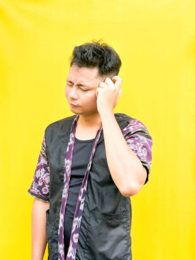 Modern etnik esinlenilmiş bir kıyafet giyen genç bir Asyalı 'nın portresi, parlak sarı bir arkaplan önünde dururken şüpheli ya da meraklı bir görünüm veriyor. Duygular, ruh hali ifadesi gibi kavramlar için mükemmel..