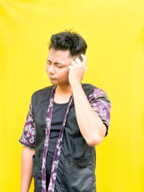 Modern etnik esinlenilmiş bir kıyafet giyen genç bir Asyalı 'nın portresi, parlak sarı bir arkaplan önünde dururken şüpheli ya da meraklı bir görünüm veriyor. Duygular, ruh hali ifadesi gibi kavramlar için mükemmel..